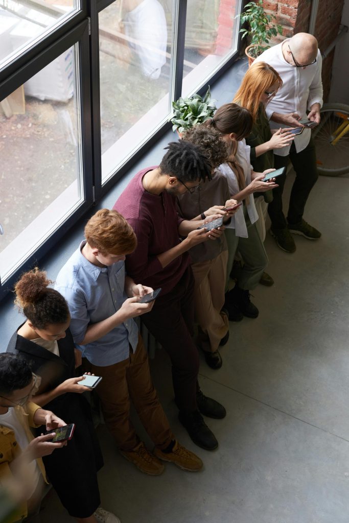 Social Media advertising A group of diverse office workers standing by a window using smartphones, capturing modern workplace connectivity.